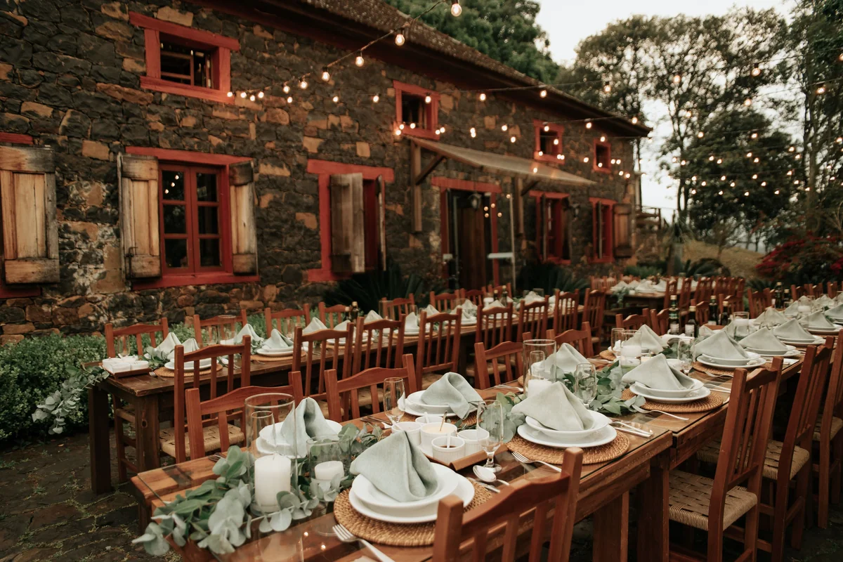 A long outdoor dinner table strung with lights beside a stone building at dusk, representative of an evening garden dinner party